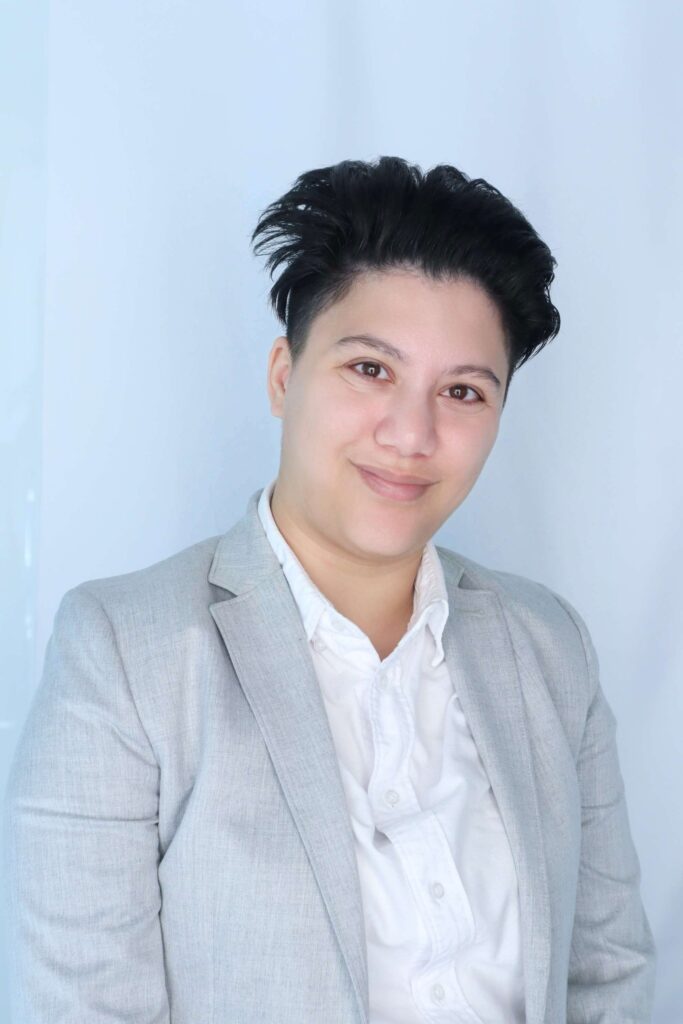 A professional photo of a woman with short black hair wearing a grey jacket and white collared shirt.