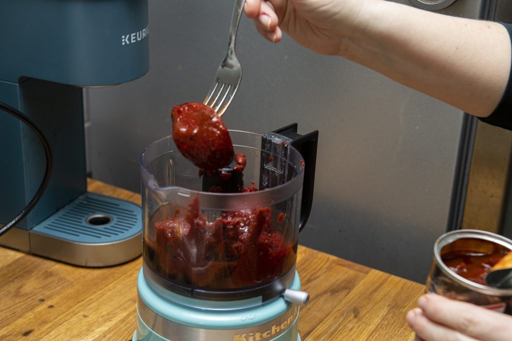 A chipotle pepper being added to a food processor