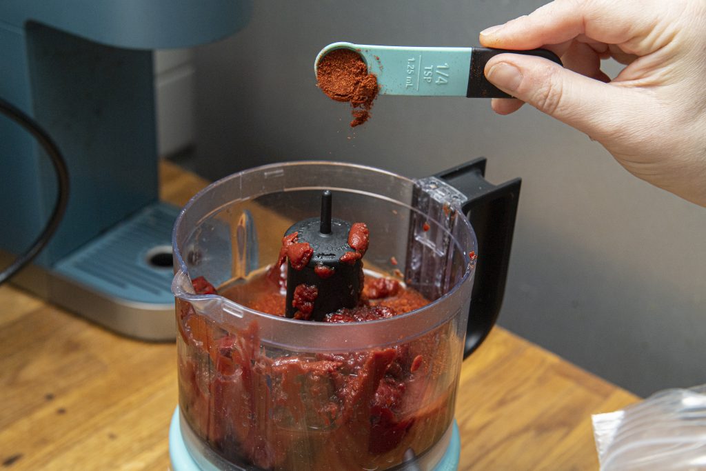 spoon of paprika being added to a food processor