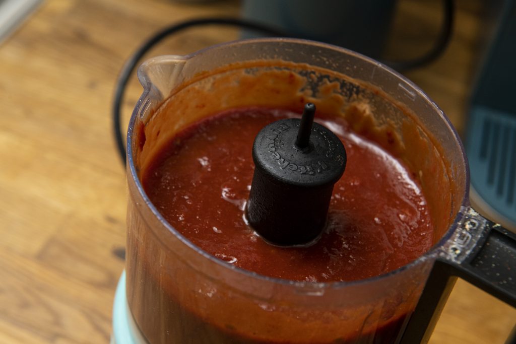 A food processor with the lid off, full of BBQ sauce