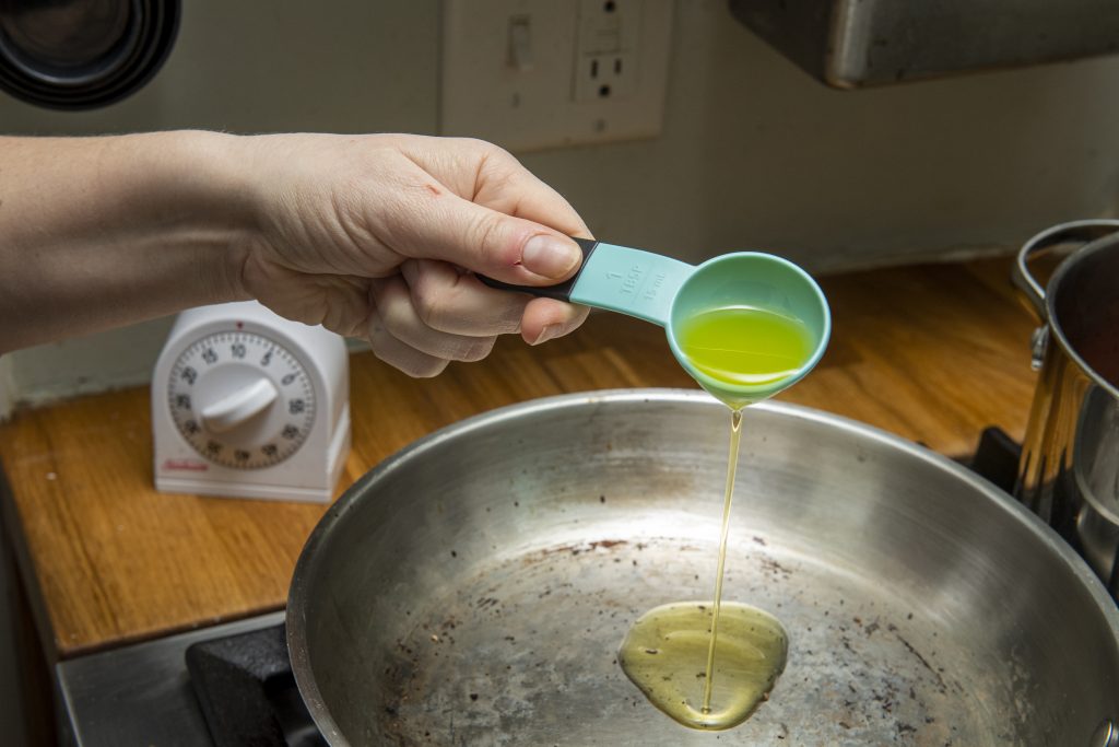 A spoonful of olive oil being poured into a pan