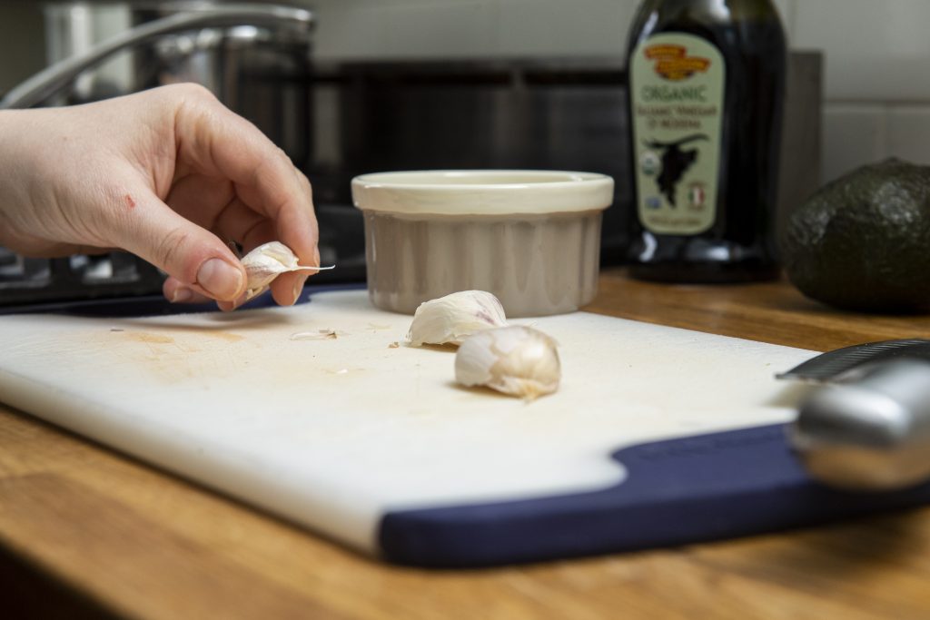 three unpeeled garlic cloves on a cutting board