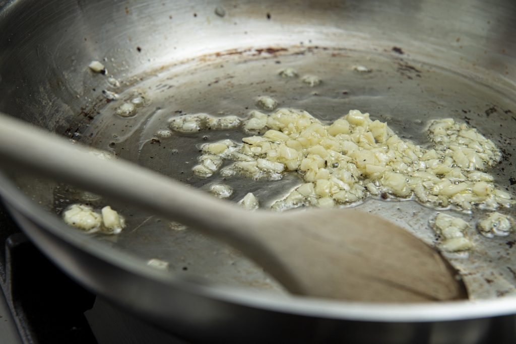 Chopped garlic in a frying pan with a wooden spoon