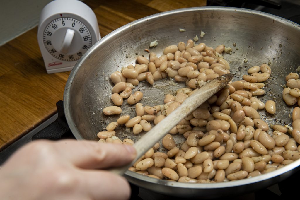 A hand holding a wooden spoon stirring a pan of beans