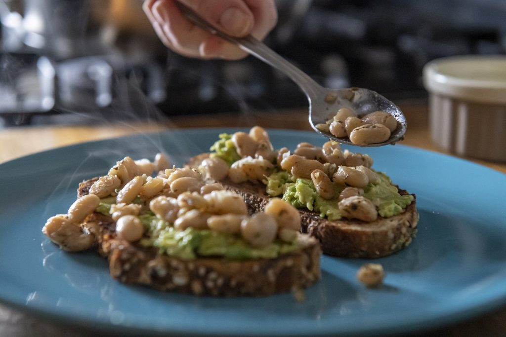 A spoon placing beans atop avocado toast