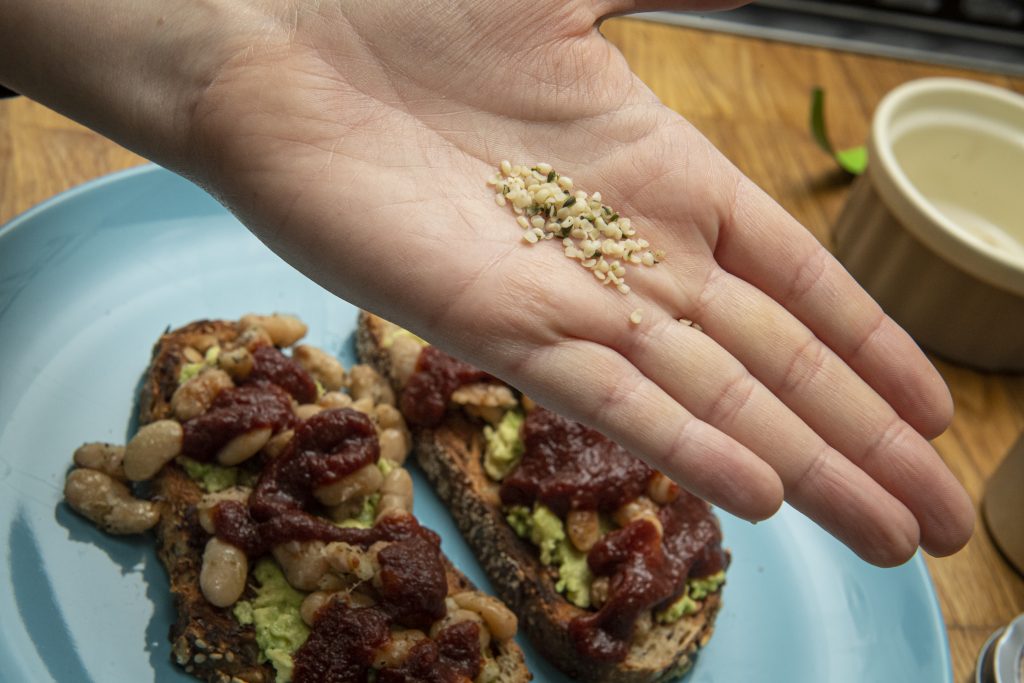 a hand holding hemp seeds, next to a plate of avocado toast