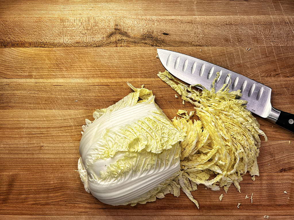 Partially shredded napa cabbage on a counter next to a knife
