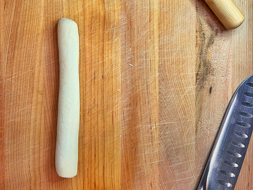 Dough rolled into a thin cylinder on a butcher block counter