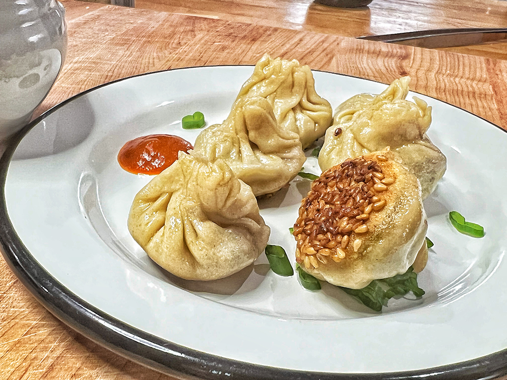 Six dumplings on a plate. One is upside down, revealing a sesame seed bottom.