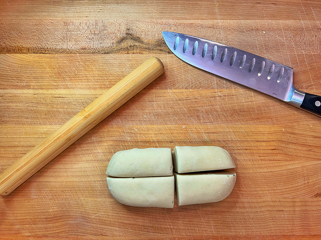 A dough ball cut into quarters next to a knife and a rolling pin.