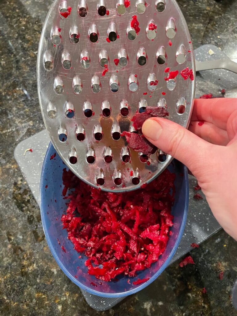 A hand holds a grater over a bowl full of grated beets.