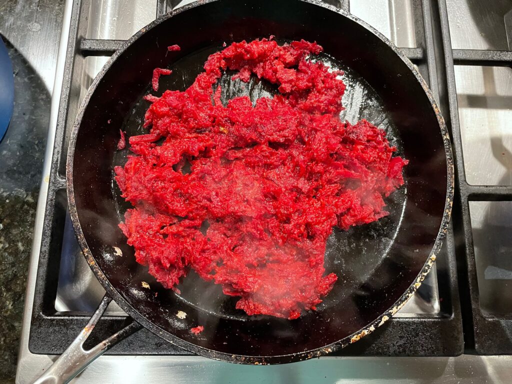 A frying pan full of grated beets cooks on a stovetop.