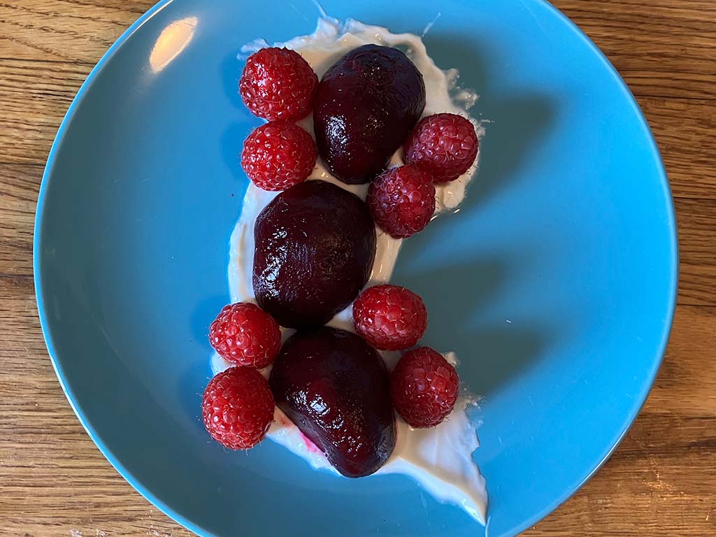 Beets and raspberries layered atop a smear of white yogurt on a blue plate.